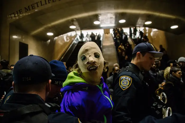 A close-up of a masked protester in the midst of other protesters and police officers at Grand Central Terminal.